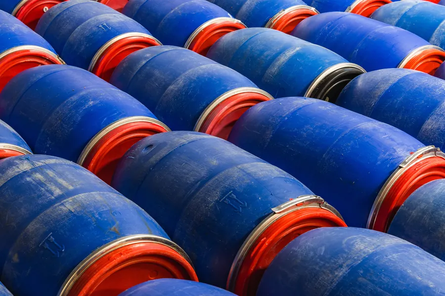 Tambores azuis armazenados em área industrial.