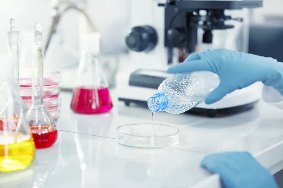 Dosagem de catalisador líquido em laboratório, com luvas de proteção.
