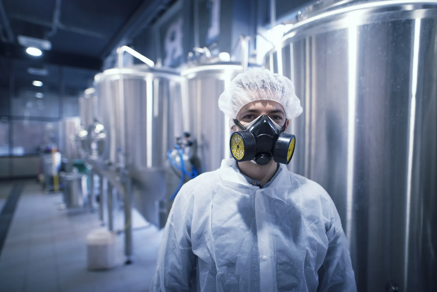 Profissional com uniforme e máscara de proteção manuseando produto químico.