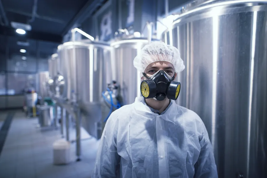 Profissional com uniforme e máscara de proteção manuseando produto químico.